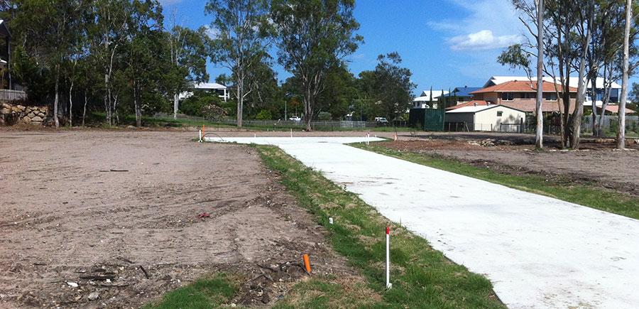 New residential subdivision site with newly constructed concrete access road, survey markers in place, cleared lots and surrounding houses, following material change of use and cadastral surveying works