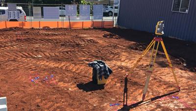 Surveyor’s total station set up on a tripod at a construction site for building setout, with marked ground points and layout lines defining foundation positions.